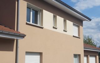 Maison individuelle rénovée avec façade beige et volets roulants blancs après travaux d’isolation extérieure